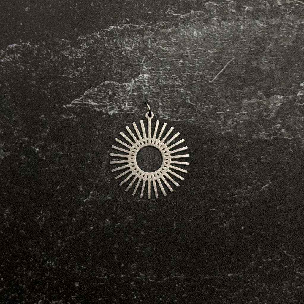 Stainless steel sun-shaped pendant on a dark textured surface