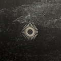 Stainless steel sun-shaped pendant on a dark textured surface