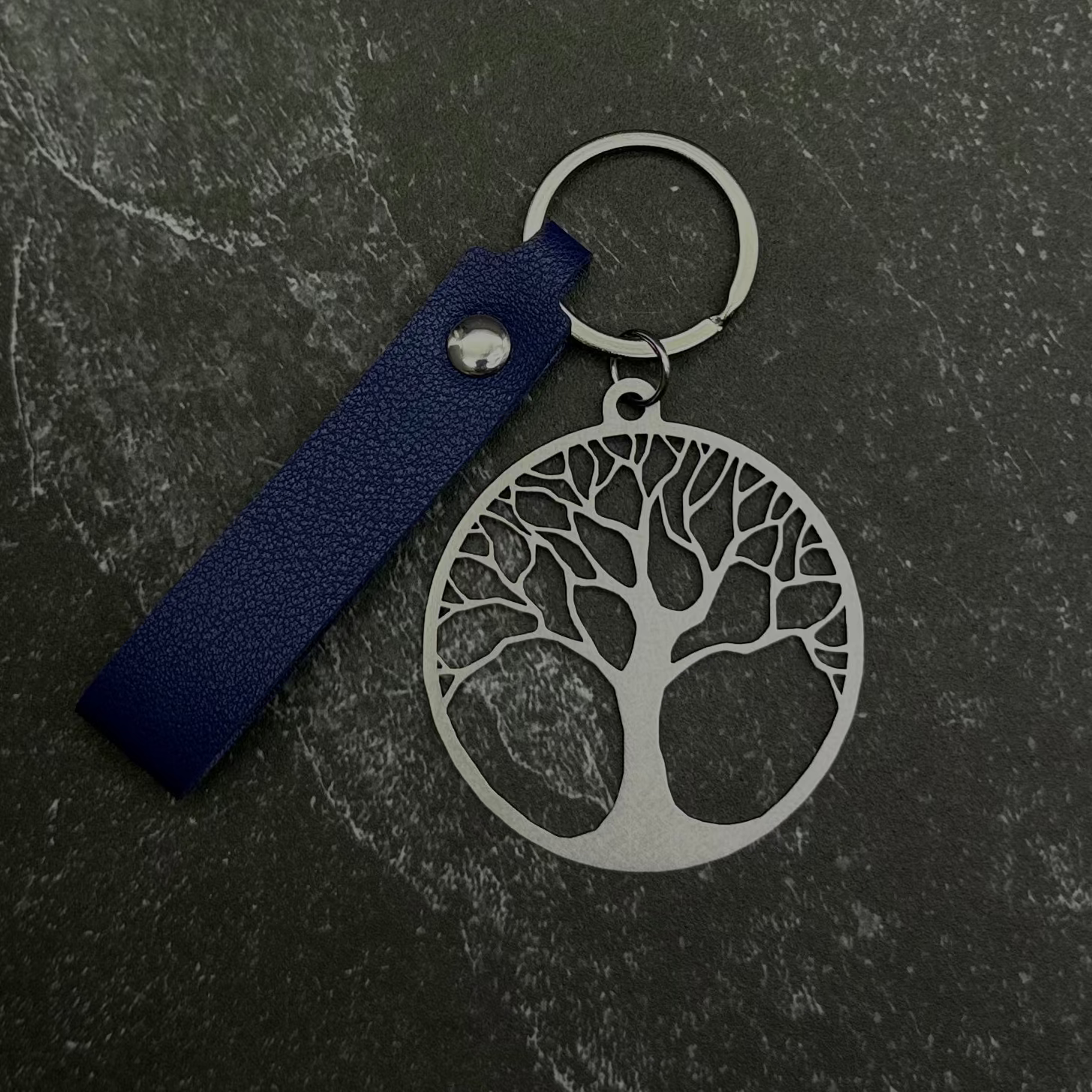 Tree of life key chain with blue leather strap on a dark surface