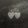 Stainless steel Heart-shaped earrings with wavy line pattern on a dark textured surface