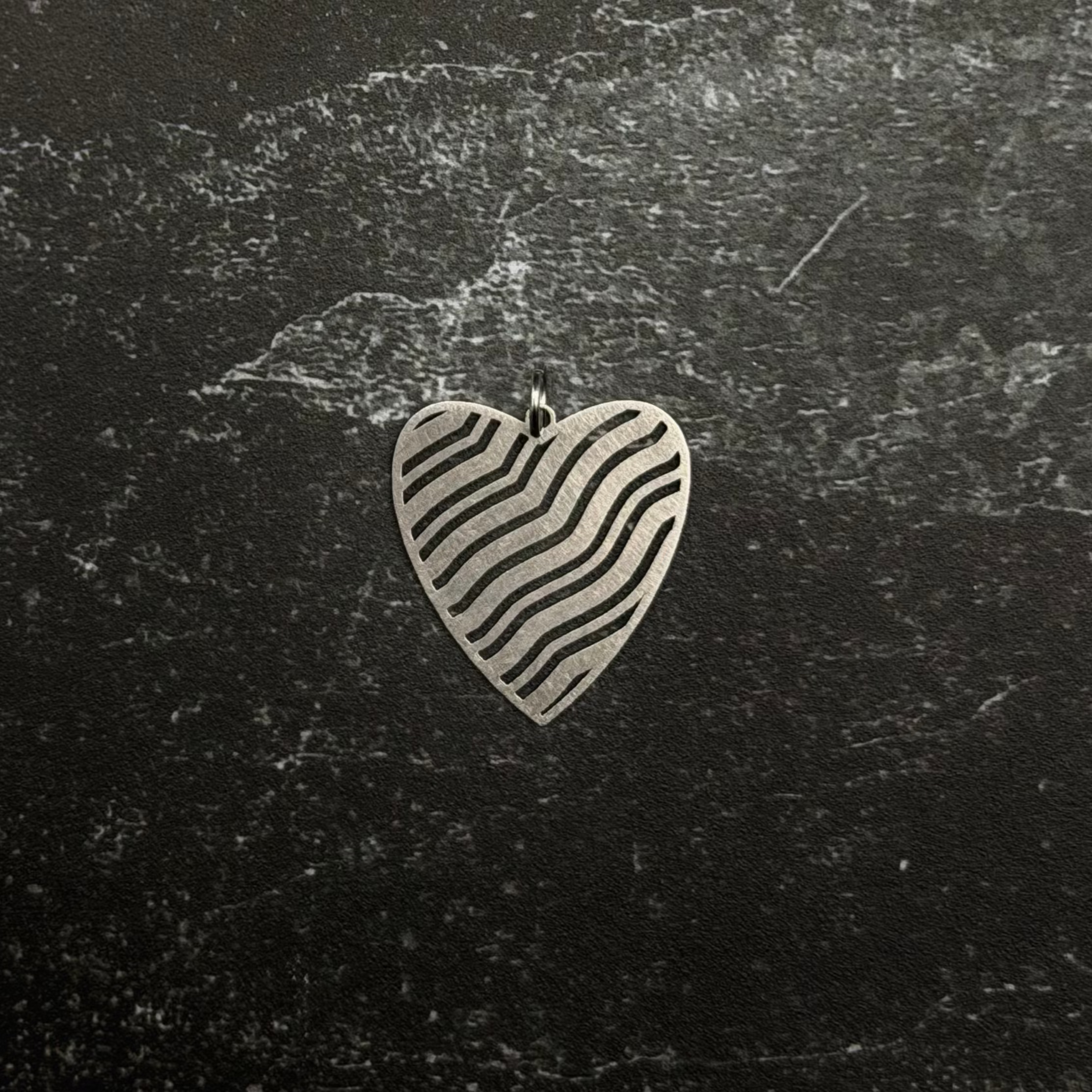 Stainless steel Heart-shaped pendant with wavy lines on a dark textured surface