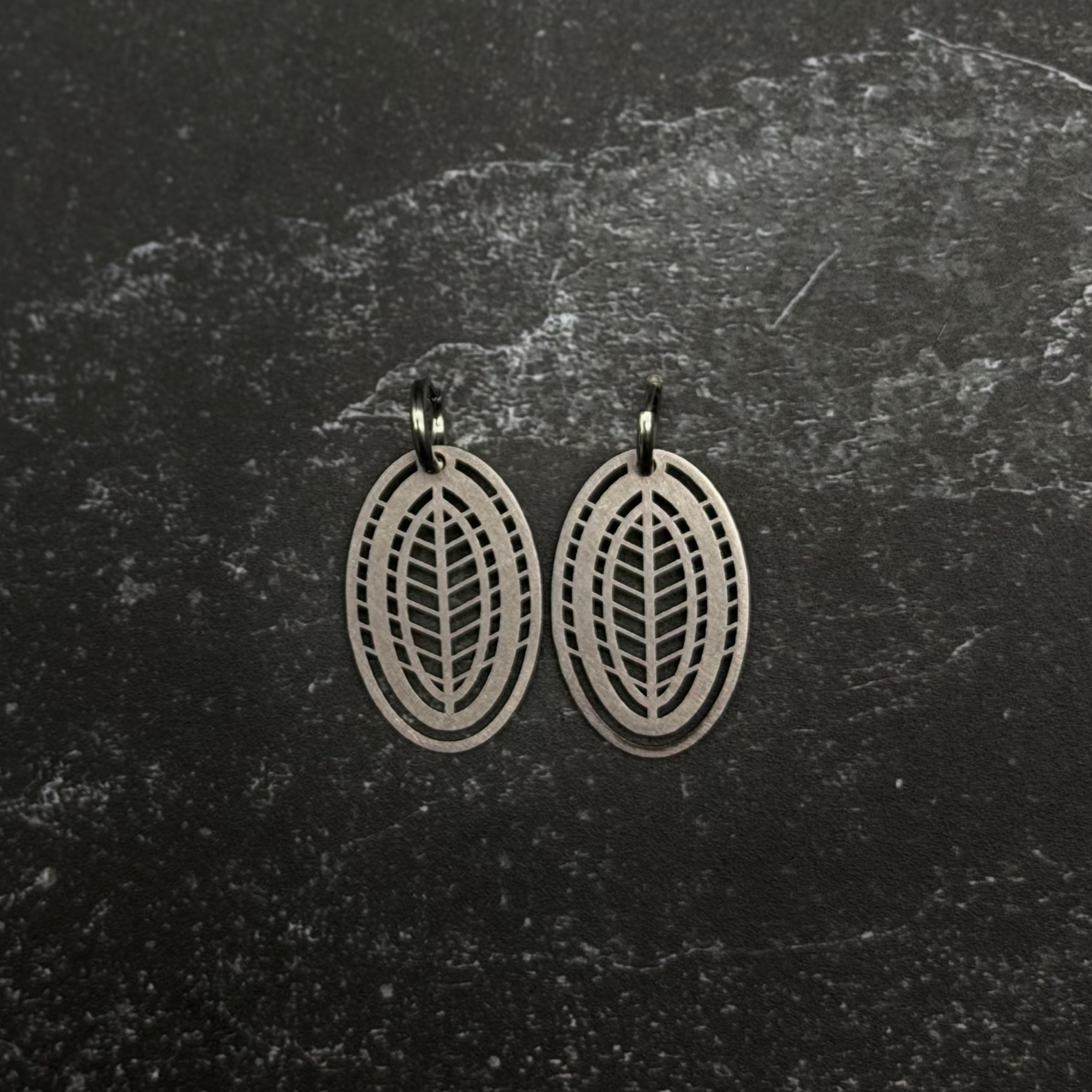 Stainless steel leaf-patterned earrings on a dark textured surface