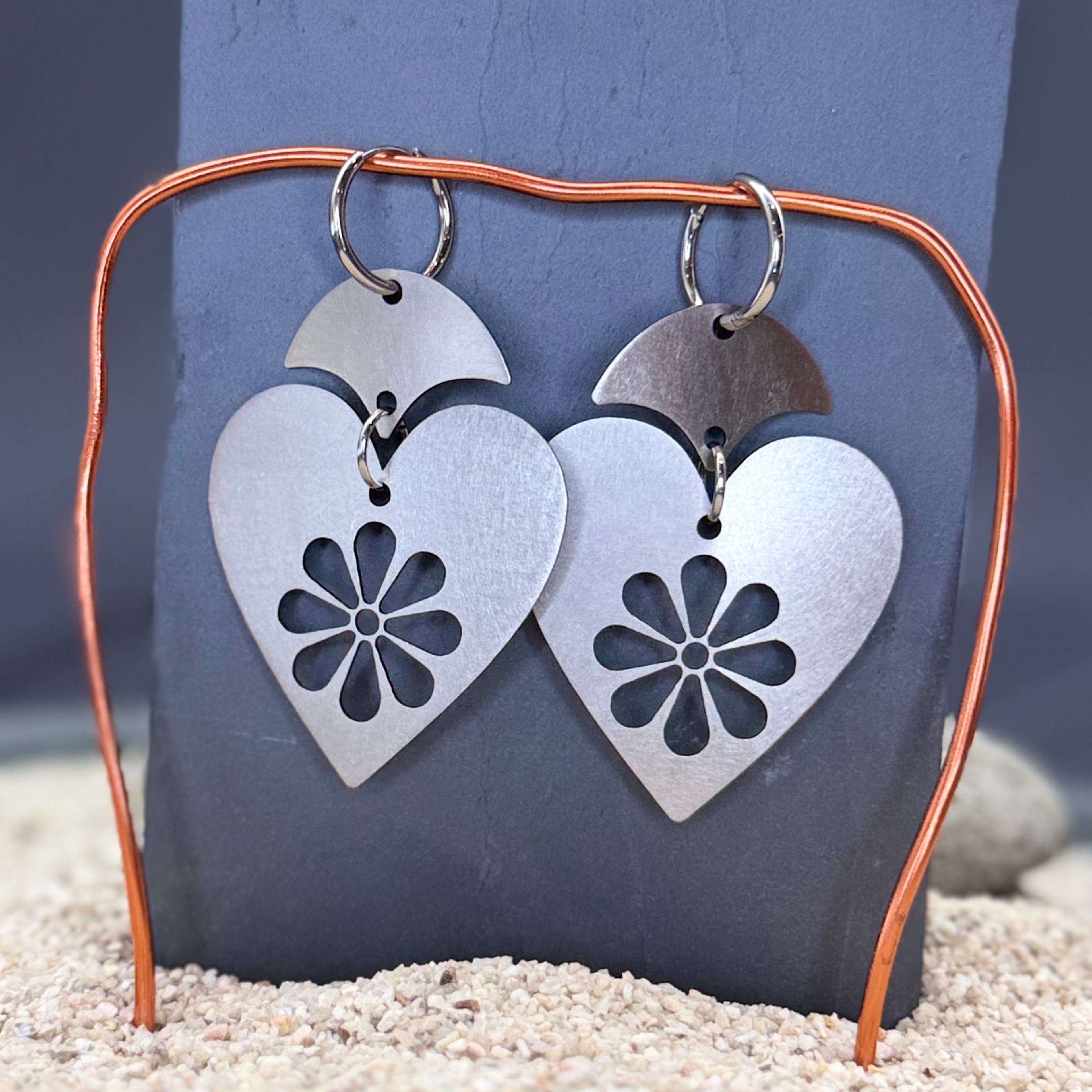 Heart-shaped metal earrings with floral design on a dark stone background