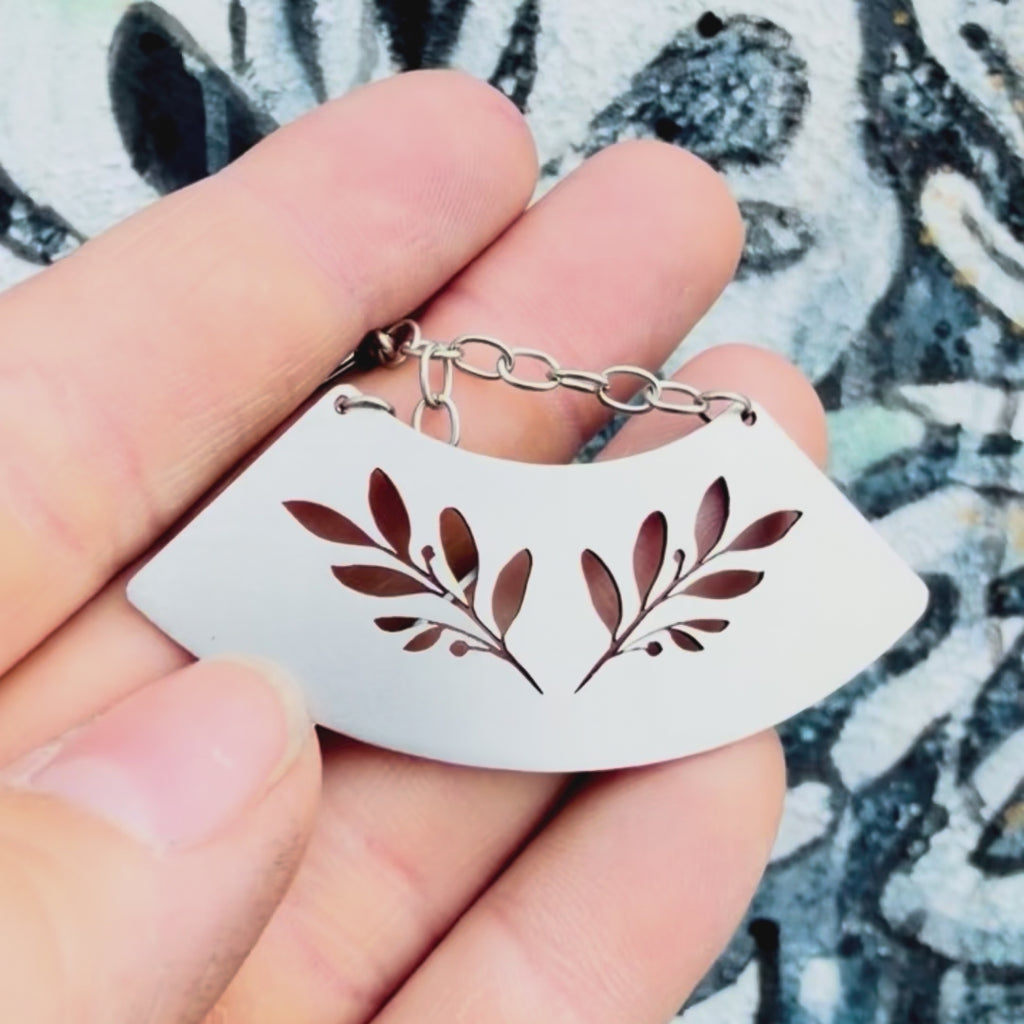 Stainless steel plant fan earring with textured background. 