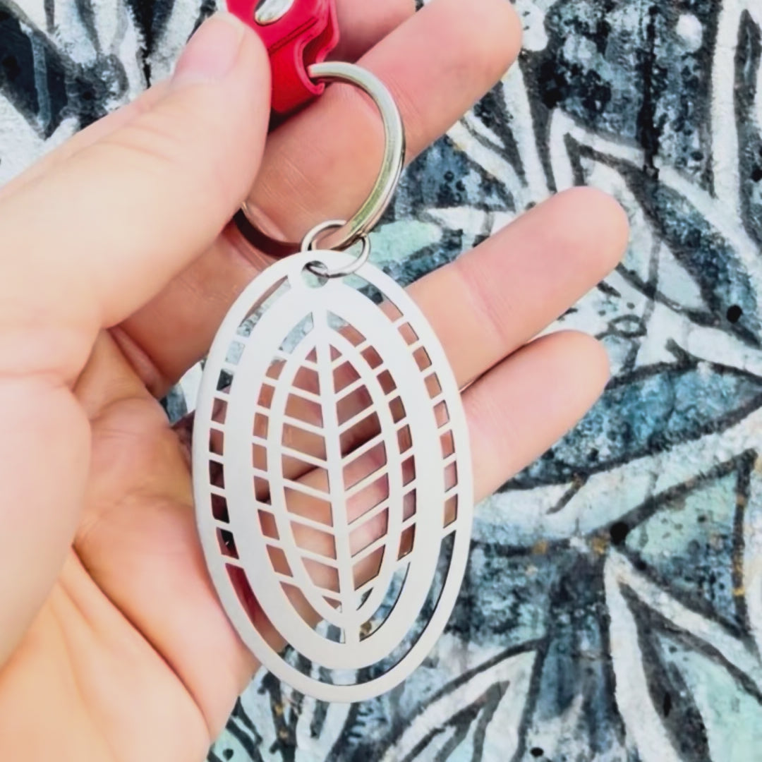Stainless steel leaf key chain with textured background. 