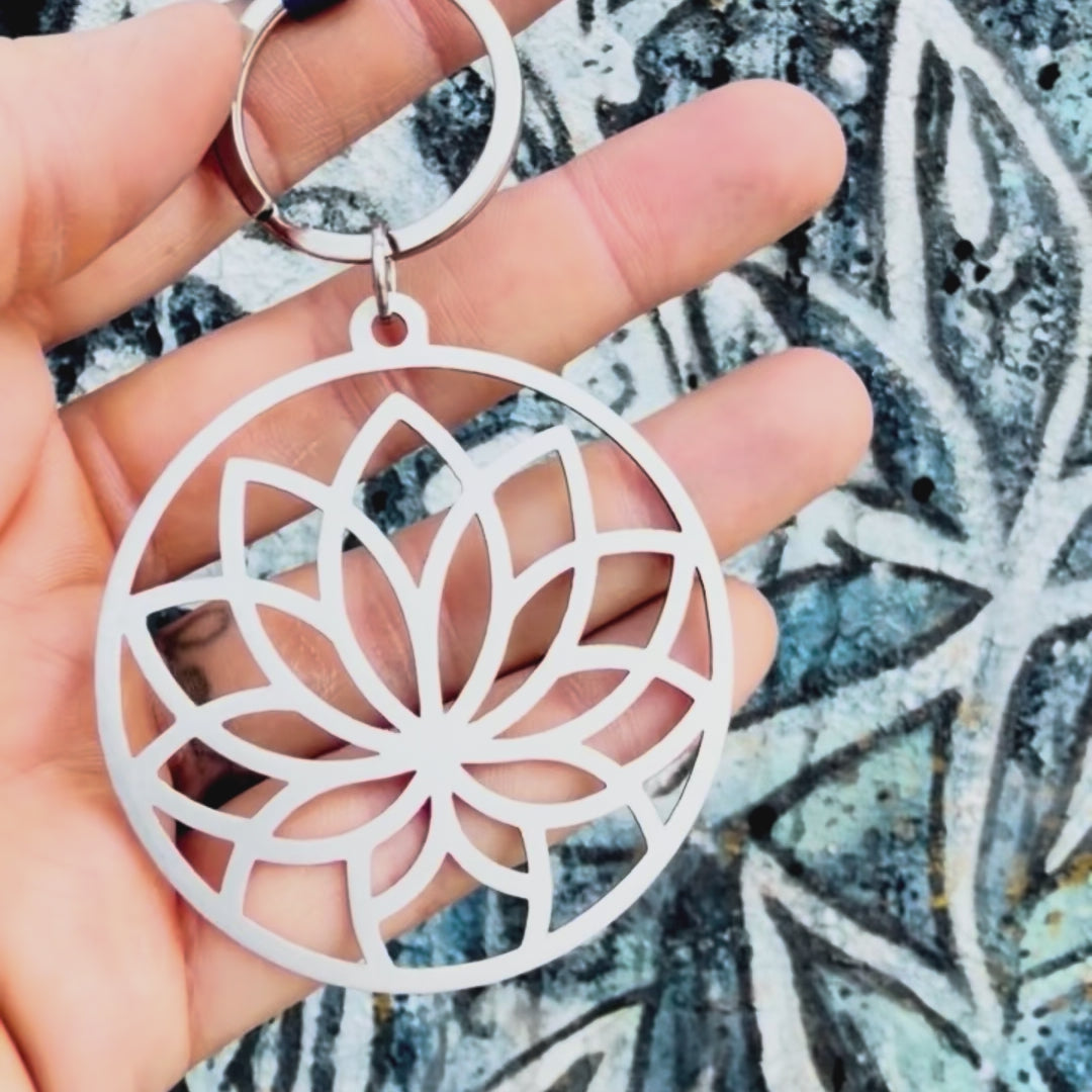 Stainless steel lotus key chain with textured background. 