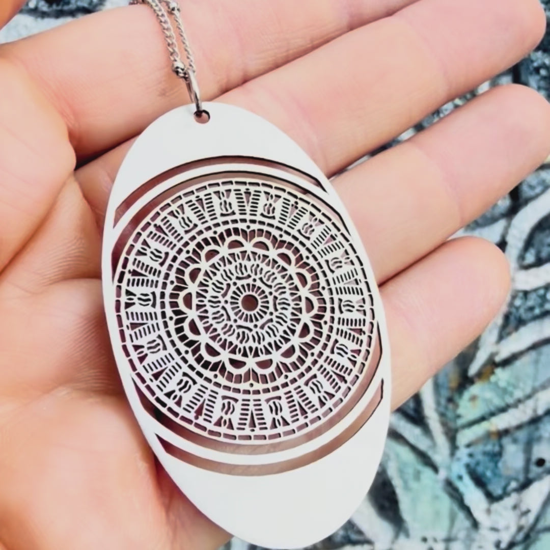 Stainless steel oval mandala pendant with textured background. 