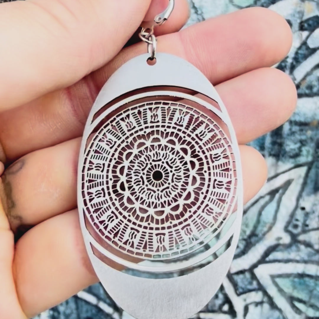 Stainless steel oval mandala earring with textured background. 