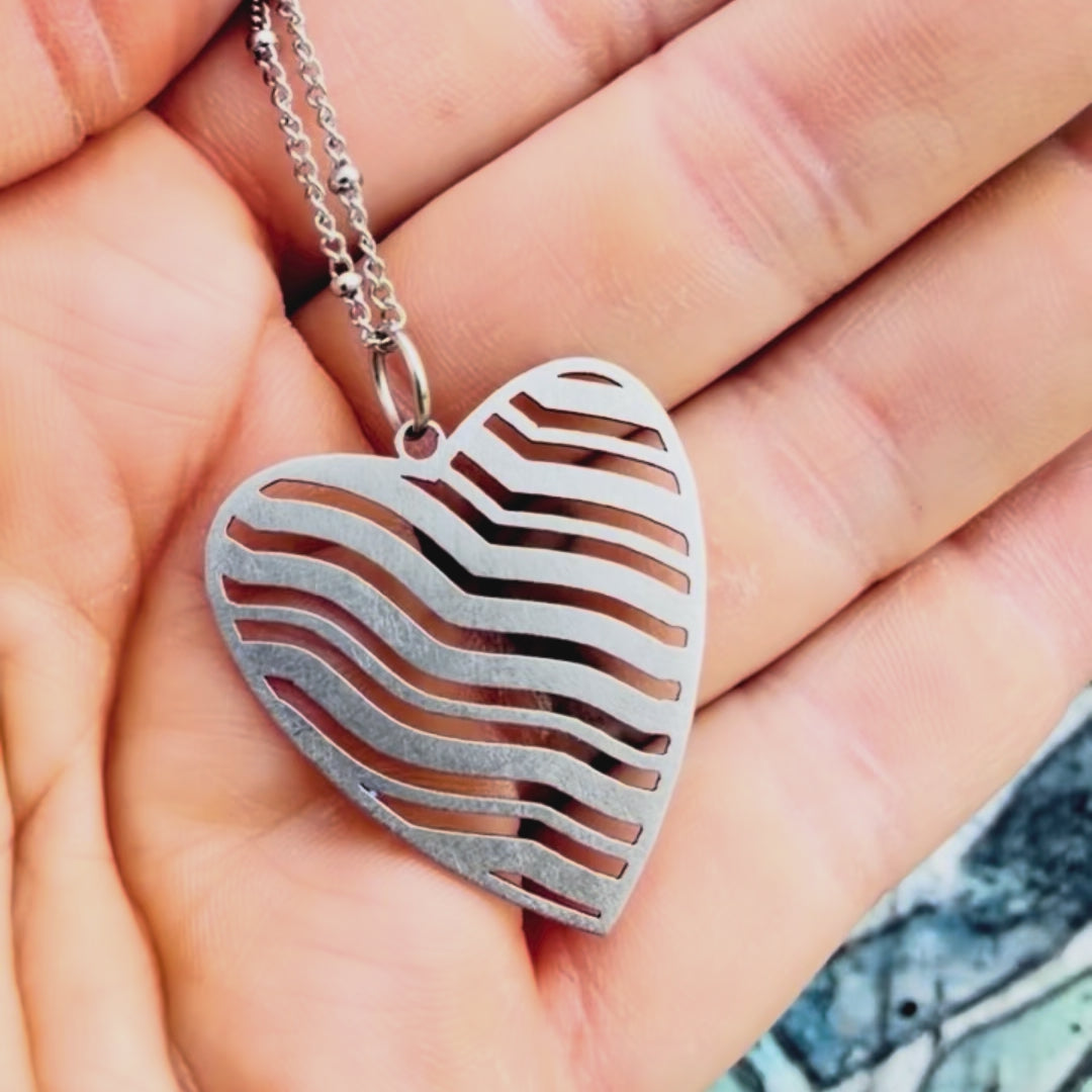 Stainless steel wavy heart pendant with textured background.