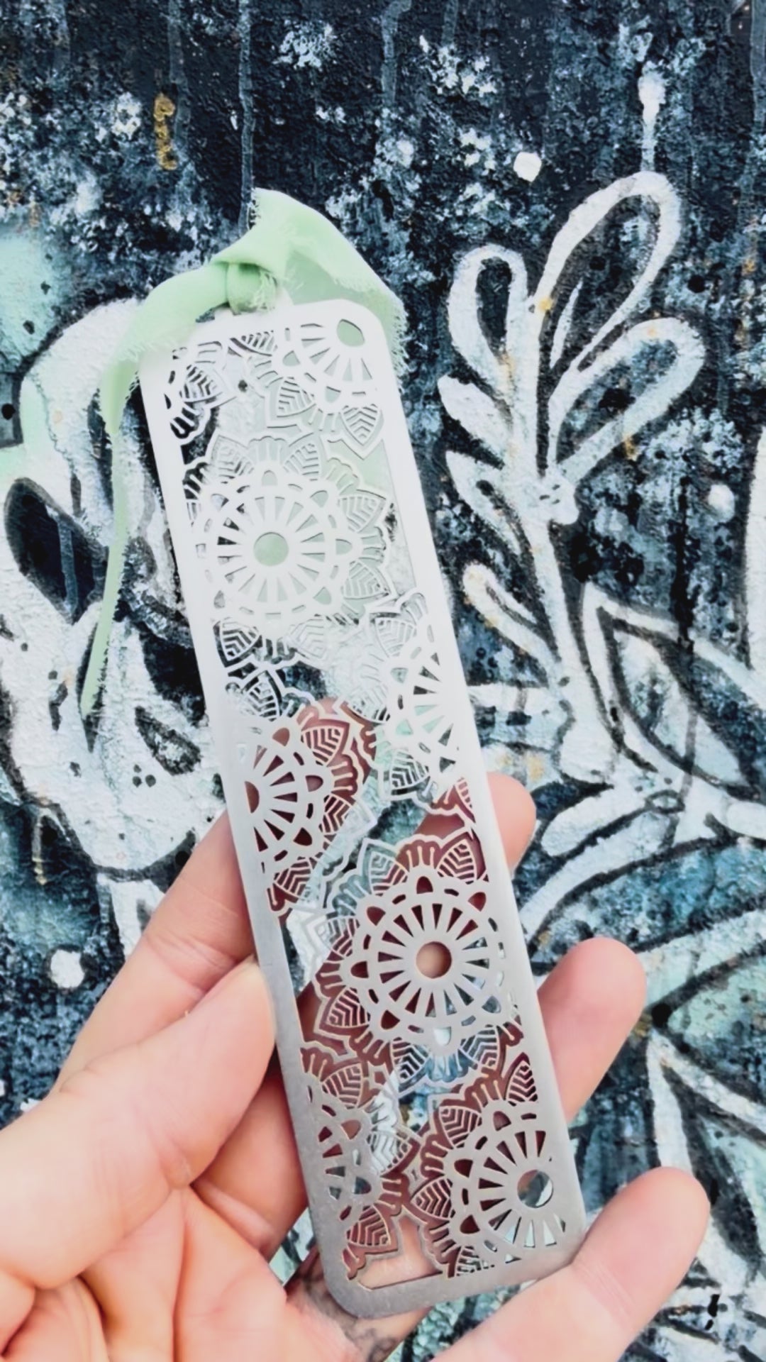 Stainless steel flower geometric mandala bookmark with textured background. 