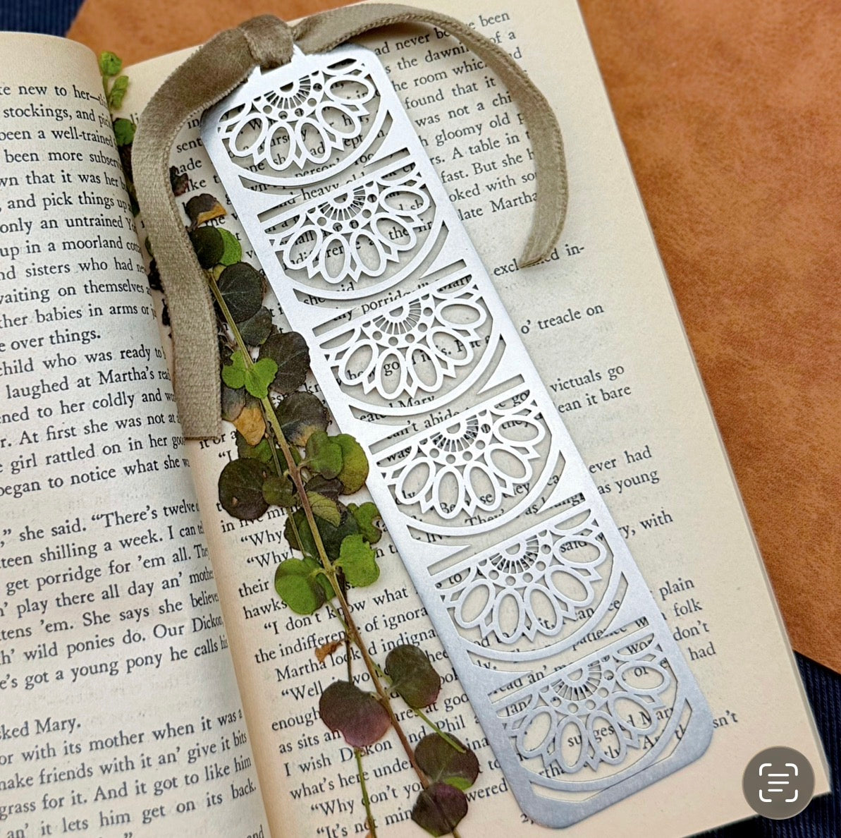 Decorative metal bookmark on an open book with a natural element.