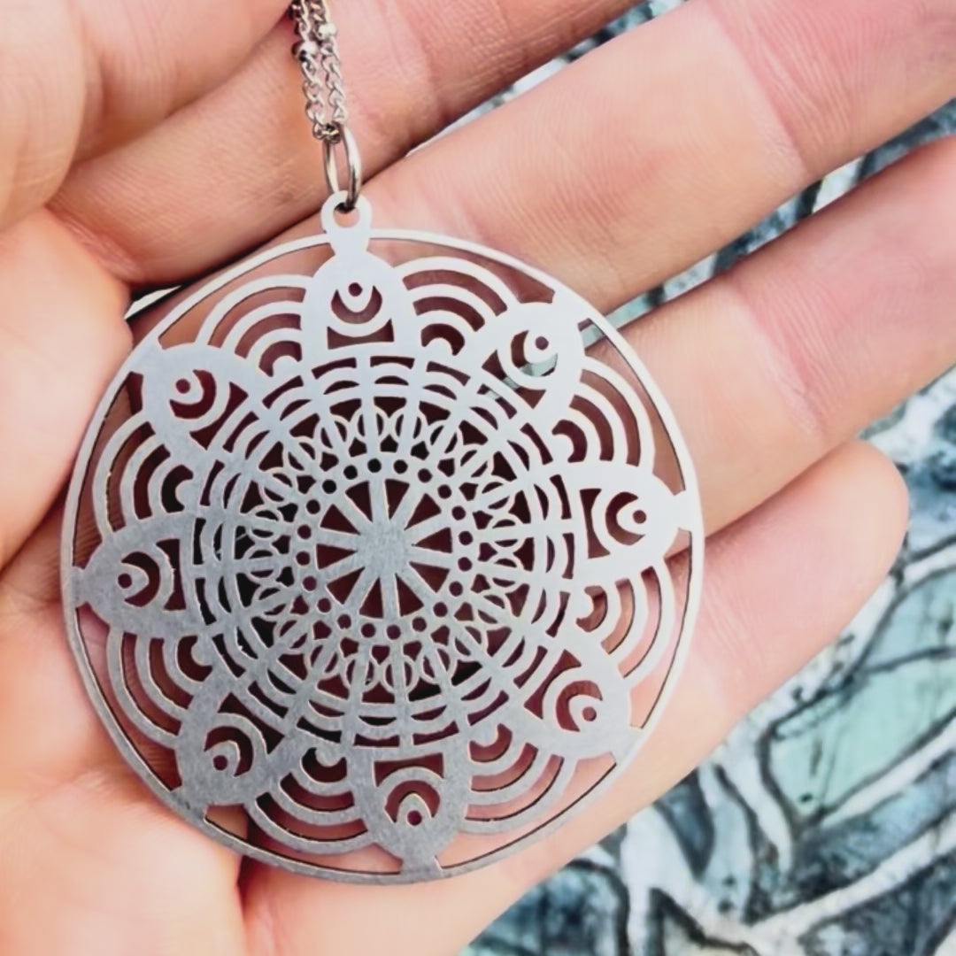 Stainless steel flower mandala pendant with textured background. 