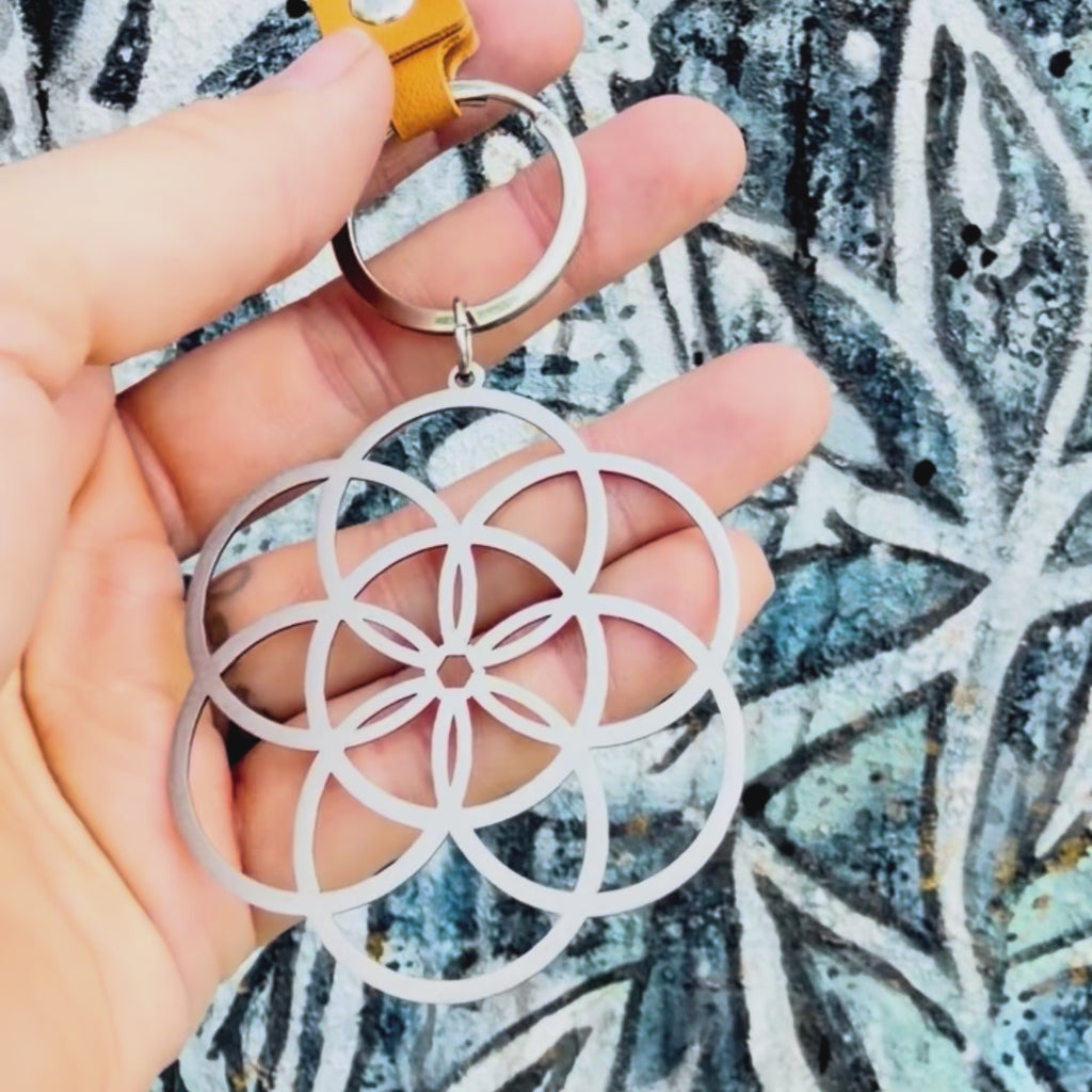 Stainless steel seed of life key chain with textured background. 