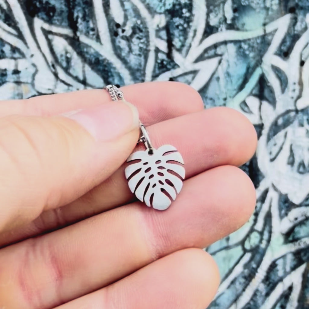 Stainless steel small monstera pendant with textured background. 