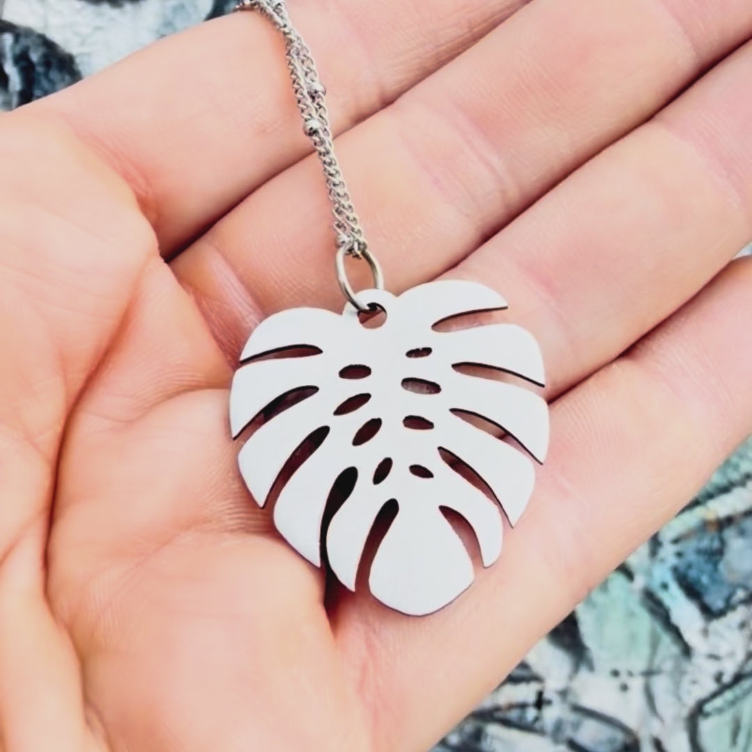 Stainless steel large monstera pendant with textured background. 