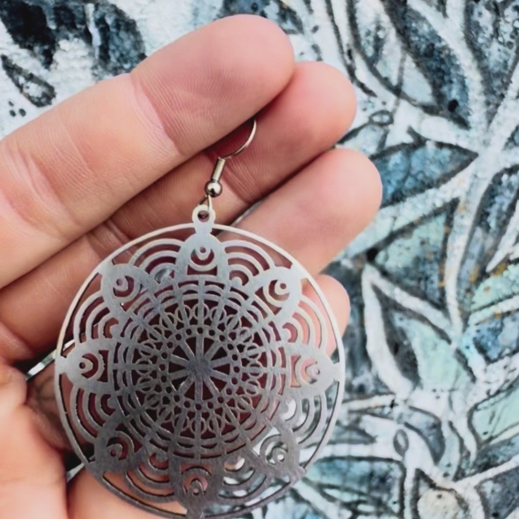 Stainless steel geometric mandala earring with textured background. 