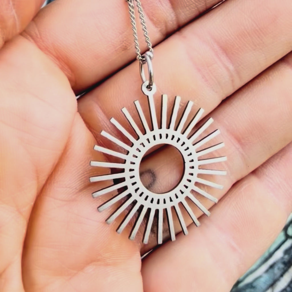 Stainless steel sunburst pendant with textured background. 