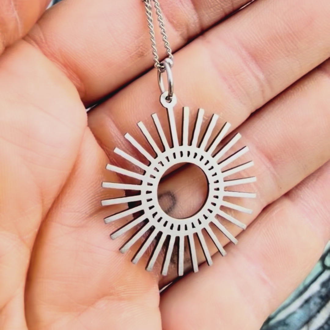 Stainless steel sunburst pendant with textured background. 