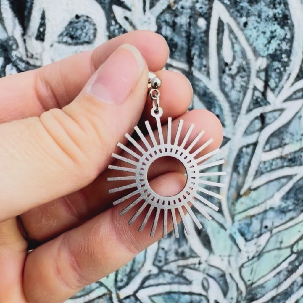 Stainless steel sunburst earring with textured background. 