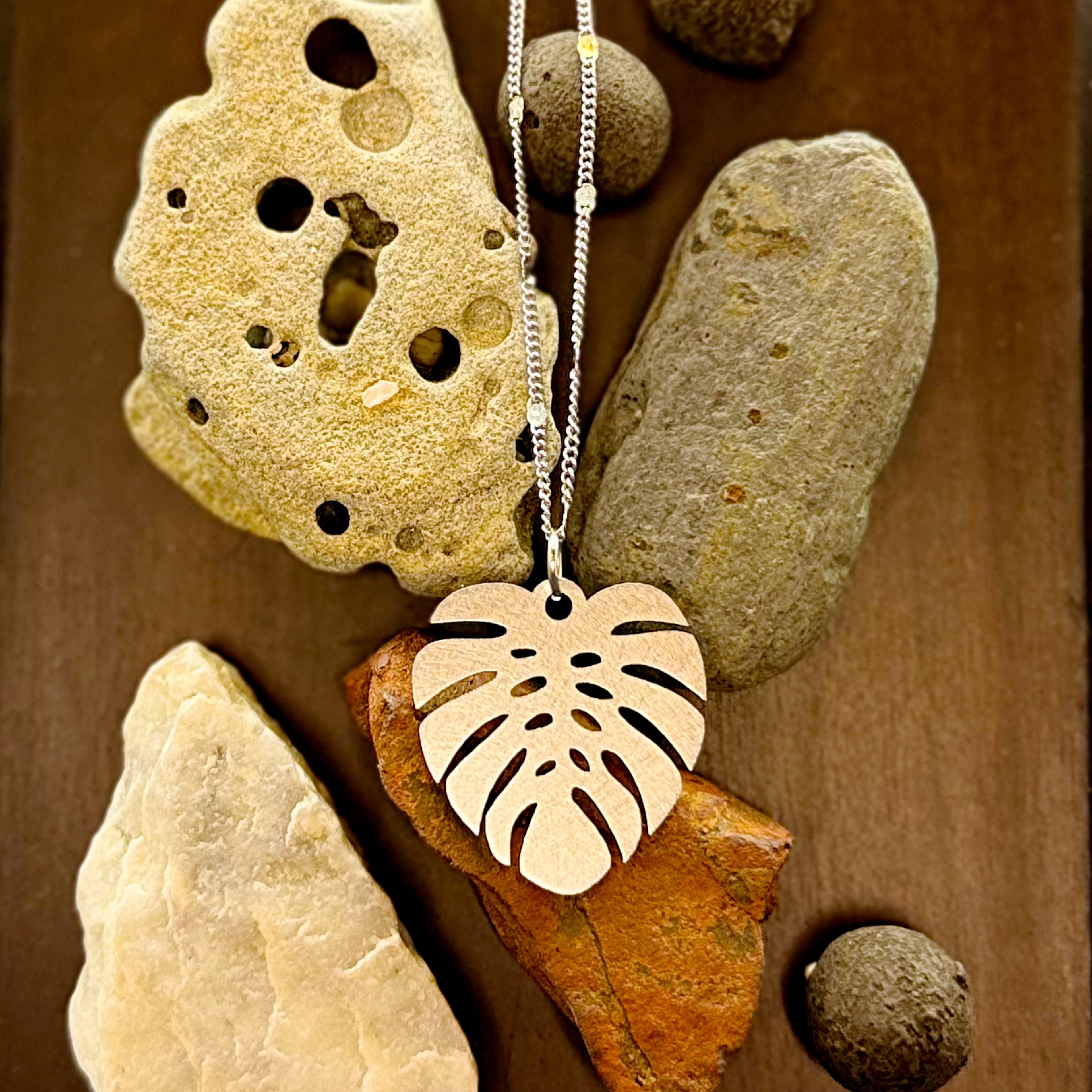 Monstera necklace on pebbles over wood. 